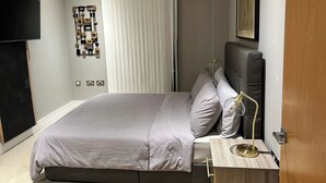A modern bedroom with a bed, bedside table, lamp, and a mounted artwork on the wall. - Luxury two bed two Bath In Excel (London)