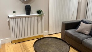 A modern living room with a radiator, a grey sofa, a round coffee table, a mirror, and a potted plant. - Luxury two bed two Bath In Excel (London)