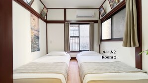 A room with two beds, a window with curtains, an air conditioning unit, and a painting on the wall.