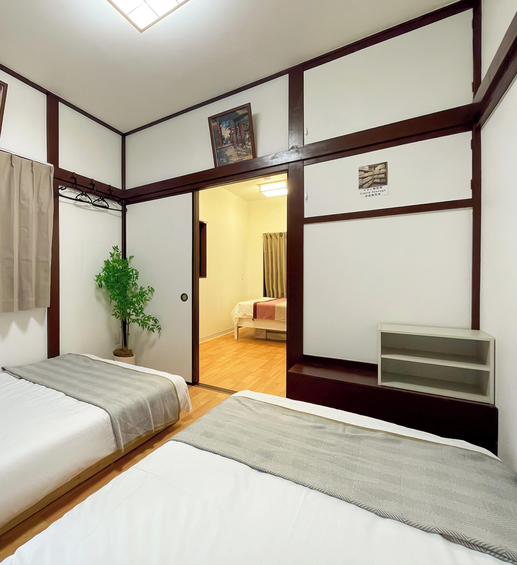 A hotel room with two beds, a potted plant, a small shelf, and a door leading to another room.