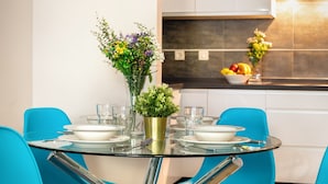 Een moderne eethoek met een glazen tafel, blauwe stoelen en een bloemenvaas.