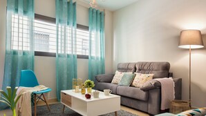 Een woonkamer met een grijze bank, een witte salontafel, een blauwe fauteuil en een vloerlamp.