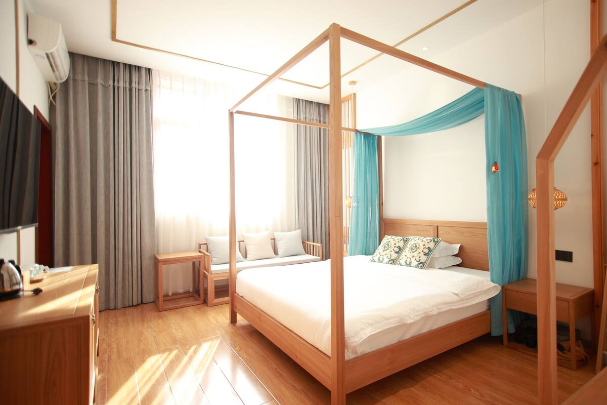 A modern hotel room with a four-poster bed, a wooden nightstand, a bedside table, and a television.