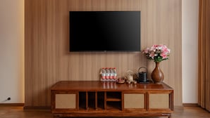 Un meuble en bois pour la télévision, avec un téléviseur à écran plat fixé au mur, un vase avec des fleurs, une théière et des bouteilles d’eau.