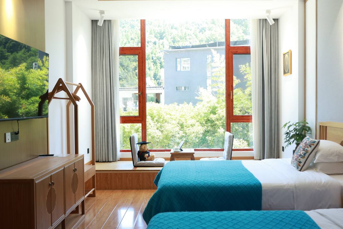 A hotel room with a bed, bedside table, and a large window with curtains.