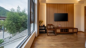 Un salon moderne doté d’une grande fenêtre, de meubles en bois et d’un téléviseur à écran plat fixé au mur.