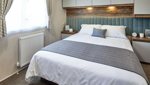 A neatly made bed with a grey blanket, a wooden headboard, and a bedside table with a clock and a picture frame. - 2 bedroom accommodation in Bishop Auckland (Bishop Auckland)