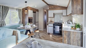 A modern kitchen with a built-in oven, a dining area with a light blue sofa, and a wooden accent wall. - 2 bedroom accommodation in Bishop Auckland (Bishop Auckland)