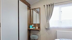 A bedroom with a bed, a window with curtains, a mirror, a small stool, and a shelf with toiletries. - 2 bedroom accommodation in Bishop Auckland (Bishop Auckland)