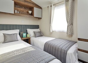 Ein Schlafzimmer mit zwei Betten, einem Holzregal mit Dekoration, einem Nachttisch mit Lampe und einem Fenster mit Vorhängen.