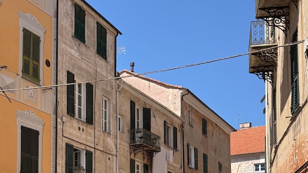 Une rue étroite bordée d’immeubles, avec des terrasses et un vélo.