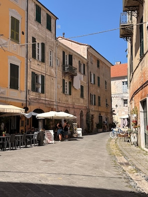 Une rue étroite bordée d’immeubles, avec des terrasses et un vélo.