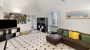 Un salon comprenant un canapé d’angle, un téléviseur à écran plat, un grand tableau abstrait et une fenêtre donnant sur des immeubles.