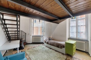 Une pièce comprenant un lit, un bureau, un radiateur, une fenêtre et un escalier.