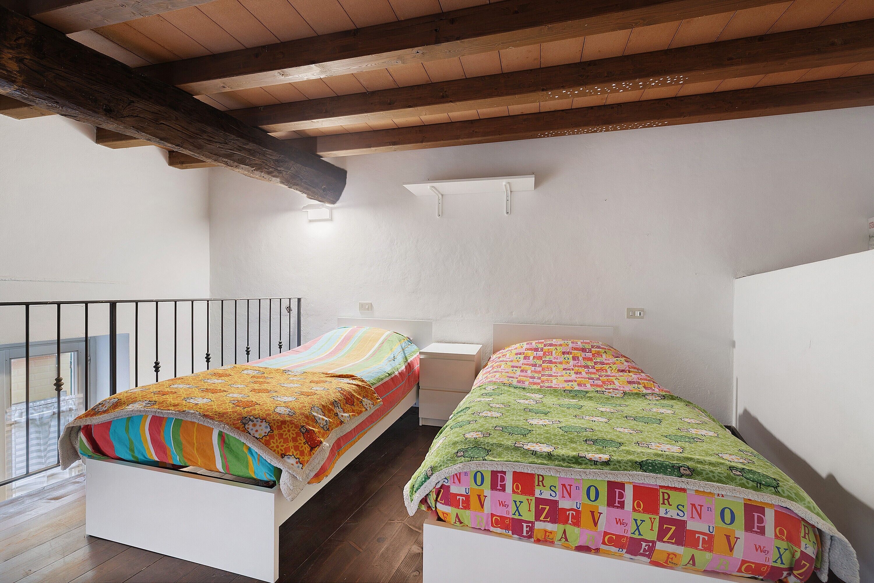 Een kamer met twee bedden, houten balken in het plafond, witte muren en een balkon.
