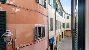Une ruelle étroite bordée de bâtiments des deux côtés, avec un lampadaire, des volets et un auvent bleu.