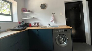 Eine kleine Küche mit Waschmaschine, Spüle und einer Uhr an der Wand.