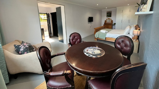Ein Schlafzimmer mit Bett, Nachttisch, Stuhl, kleinem Tisch mit Dekoration und einem Fernseher an der Wand.