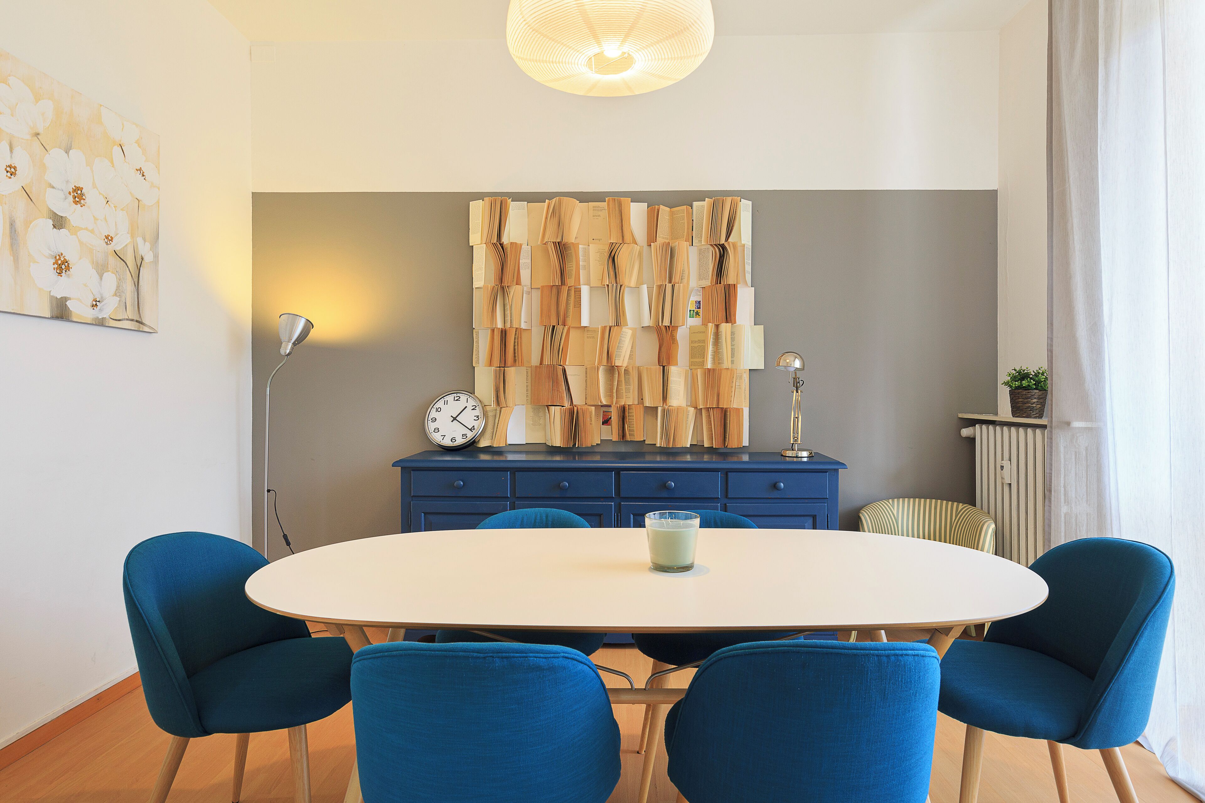 A modern dining area with a round table, four blue chairs, a clock, and a wall art piece.