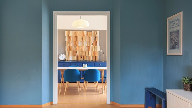 Una stanza con un tavolo e sedie in legno, un armadietto bianco e un muro blu.