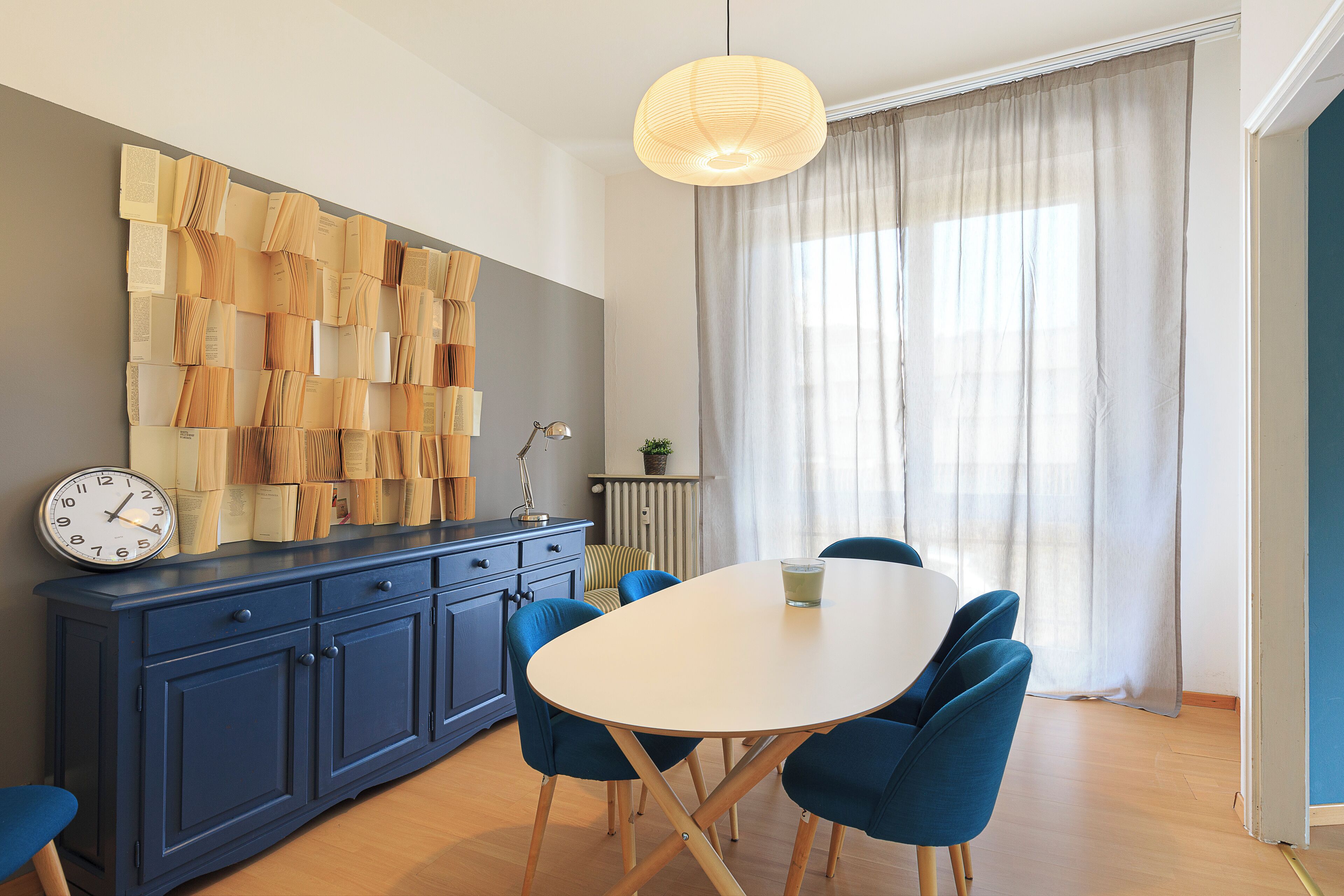 Un espace repas moderne avec une table blanche, des chaises bleues, un buffet bleu et une horloge murale.