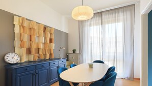 Un'area pranzo moderna con tavolo bianco, sedie blu, un armadietto blu e un orologio appeso al muro.