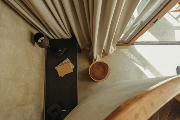 A top-down view of a room with a wooden floor, a dark-colored sofa, a small table with a bowl, and a window with curtains. - The Iggy (Cemagi)