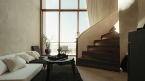 A modern living room with a sofa, a coffee table, and a staircase leading to a balcony. - The Iggy (Cemagi)