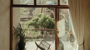 A room with a large window overlooking a rural landscape, a potted plant, and a chair. - The Iggy (Cemagi)