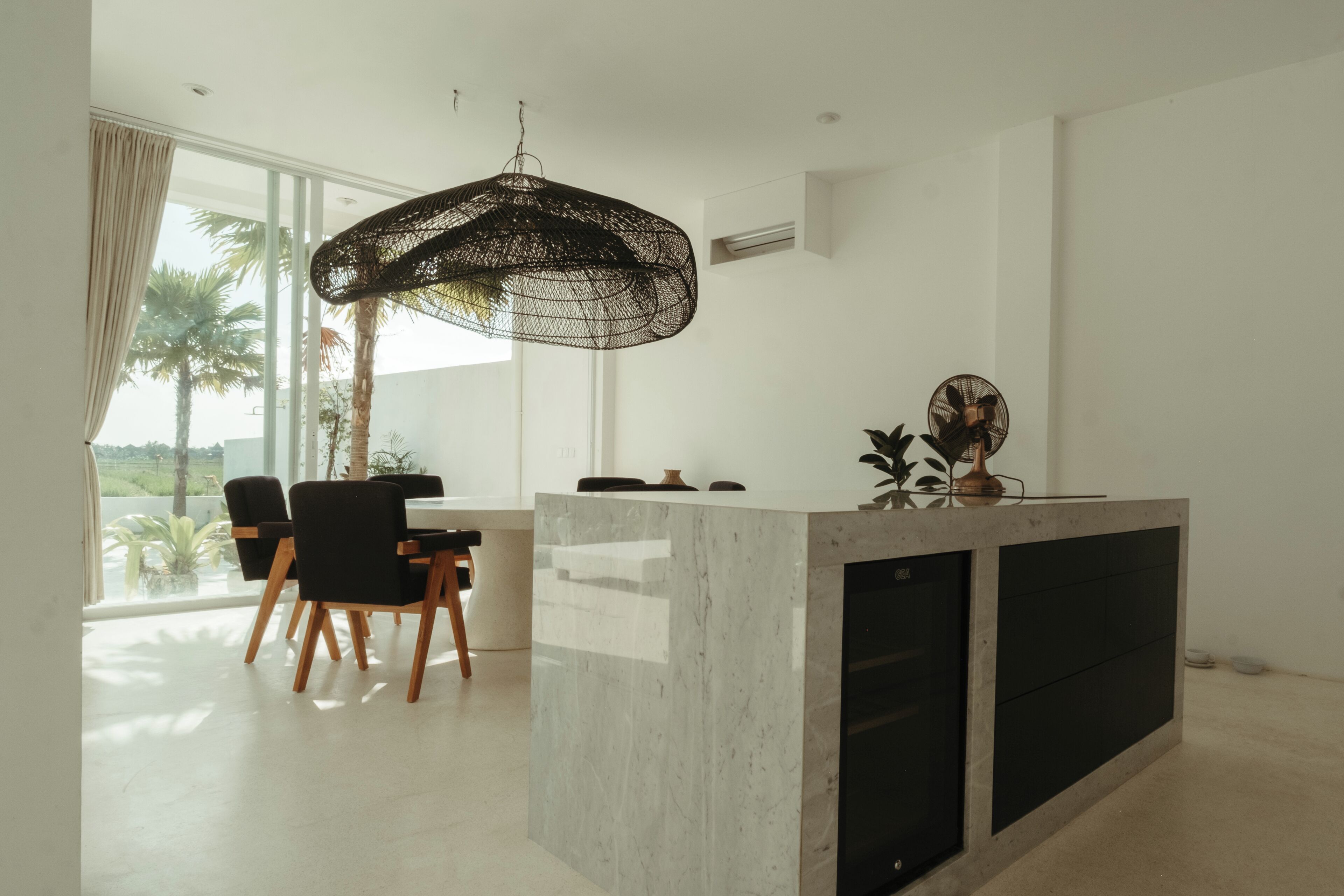 A modern kitchen with a marble island, black chairs, and a hanging light fixture.