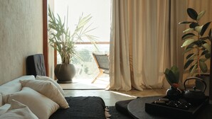 A bedroom with a bed, a side table with a teapot, a potted plant, and a view of the outdoors through a window. - The Iggy (Cemagi)