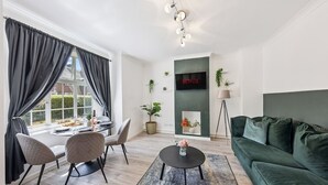 Ett modernt vardagsrum med en matplats, en grön soffa, en platt-TV och en öppen spis.