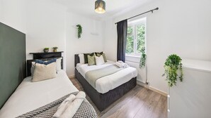 Ett modernt sovrum med två sängar, ett fönster med gardiner, en hängande växt och en taklampa.