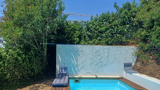 A small outdoor swimming pool with a wooden deck and a lounge chair. - Unique Large Home in Estoril with Pool - Perfect for Families (Estoril)