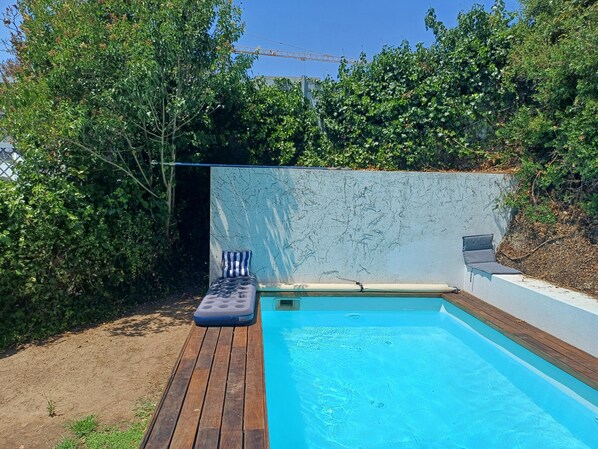 A small outdoor swimming pool with a wooden deck and a lounge chair. - Serene 3-bedroom house in Estoril perfect for relaxing getaways (Estoril)