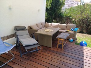 A wooden deck with a wicker sofa, a folding chair, and a small table. - Serene 3-bedroom house in Estoril perfect for relaxing getaways (Estoril)