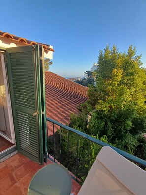 A balcony with a green door, a red-tiled roof, and lush greenery in the background. - Unique Large Home in Estoril with Pool - Perfect for Families (Estoril)