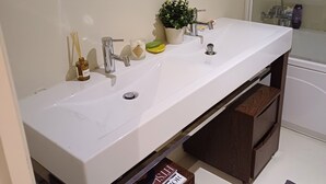 A bathroom with a double sink, a mirror above the sink, a potted plant, and a shower area. - Unique Large Home in Estoril with Pool - Perfect for Families (Estoril)