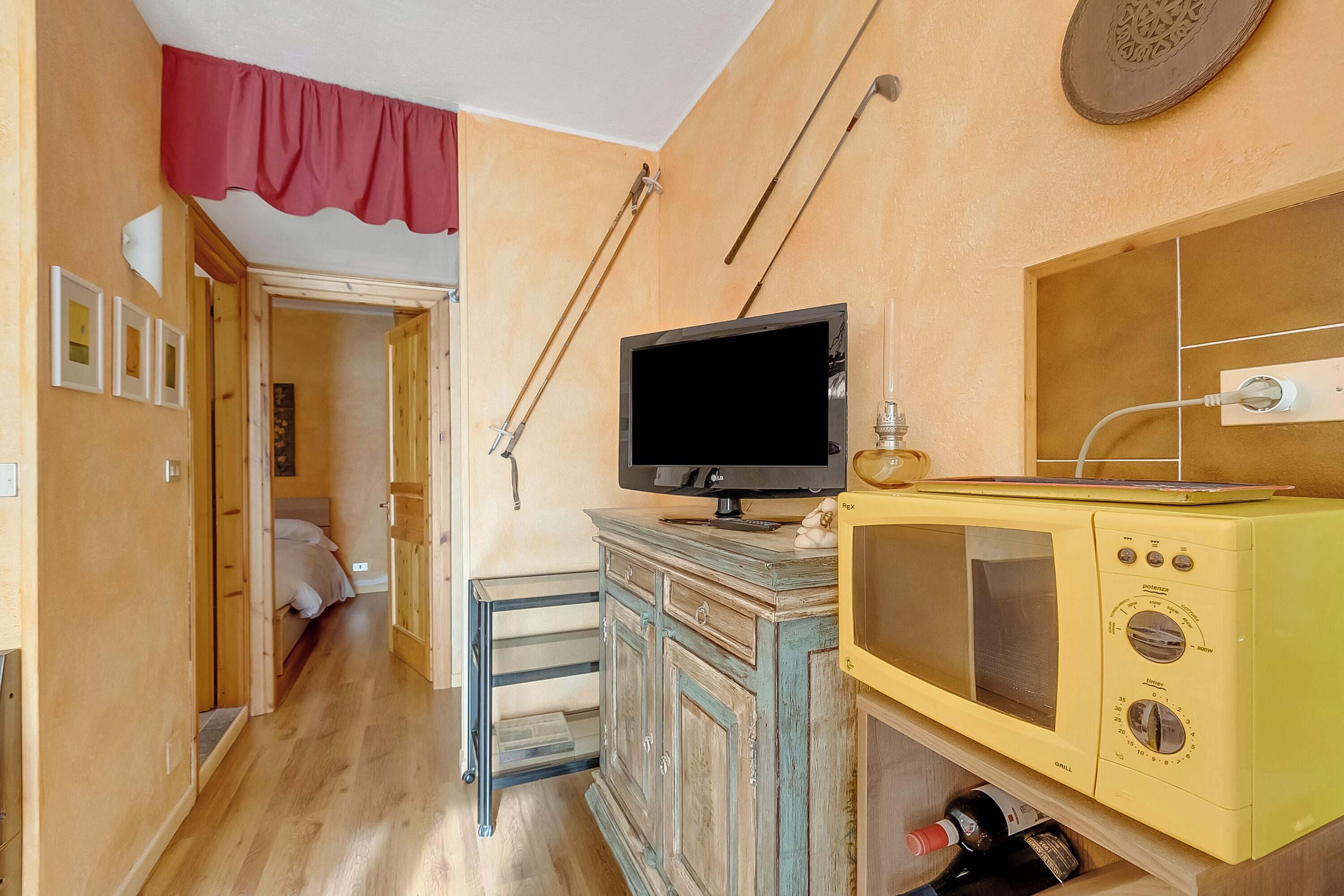 A room with a wooden floor, a bed, a television on a cabinet, and a microwave.