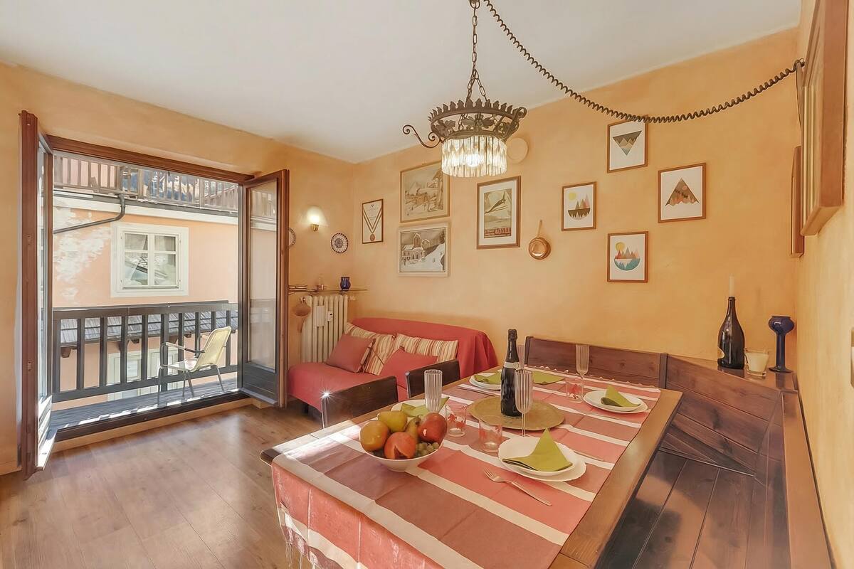 A room with a dining table set for two, a sofa, a balcony with a chair, and various wall decorations.