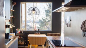 Uma cozinha compacta com uma mesa de madeira, uma janela com vista para árvores e um lustre.