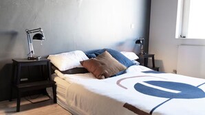 Quarto com uma cama, duas mesinhas de cabeceira, uma luminária em cada mesa e uma janela.