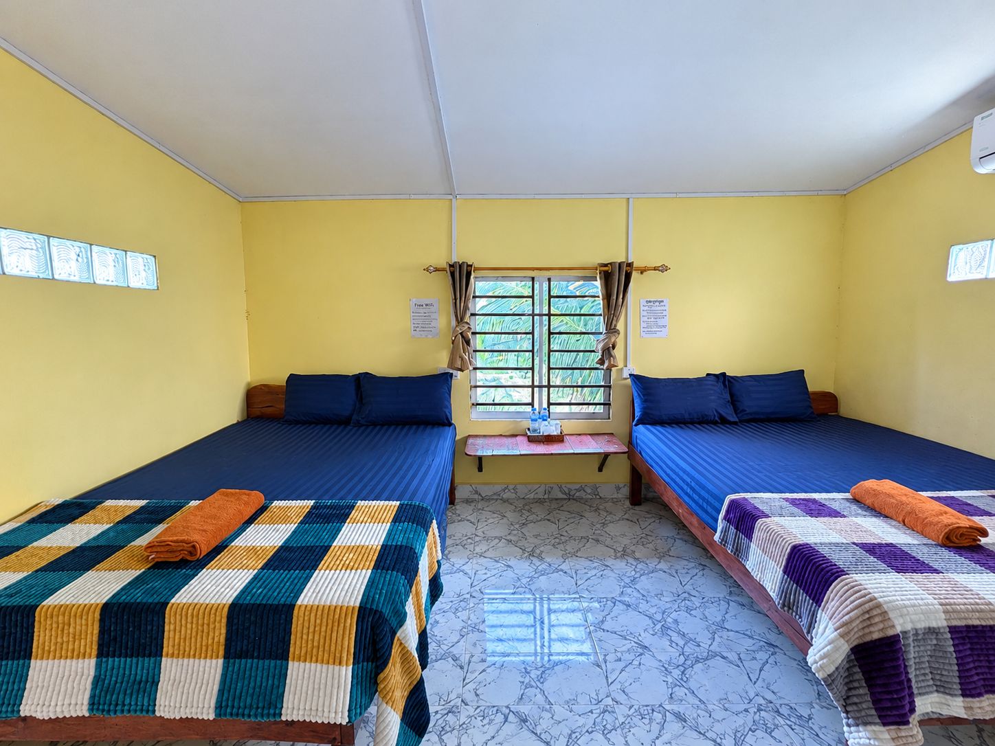 A hotel room with two beds, a window with curtains, a small table with a tray, and a tiled floor.