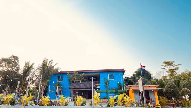 A blue building with a flag, surrounded by tropical plants. - Para Hostel Koh Rong (Koh Rong)