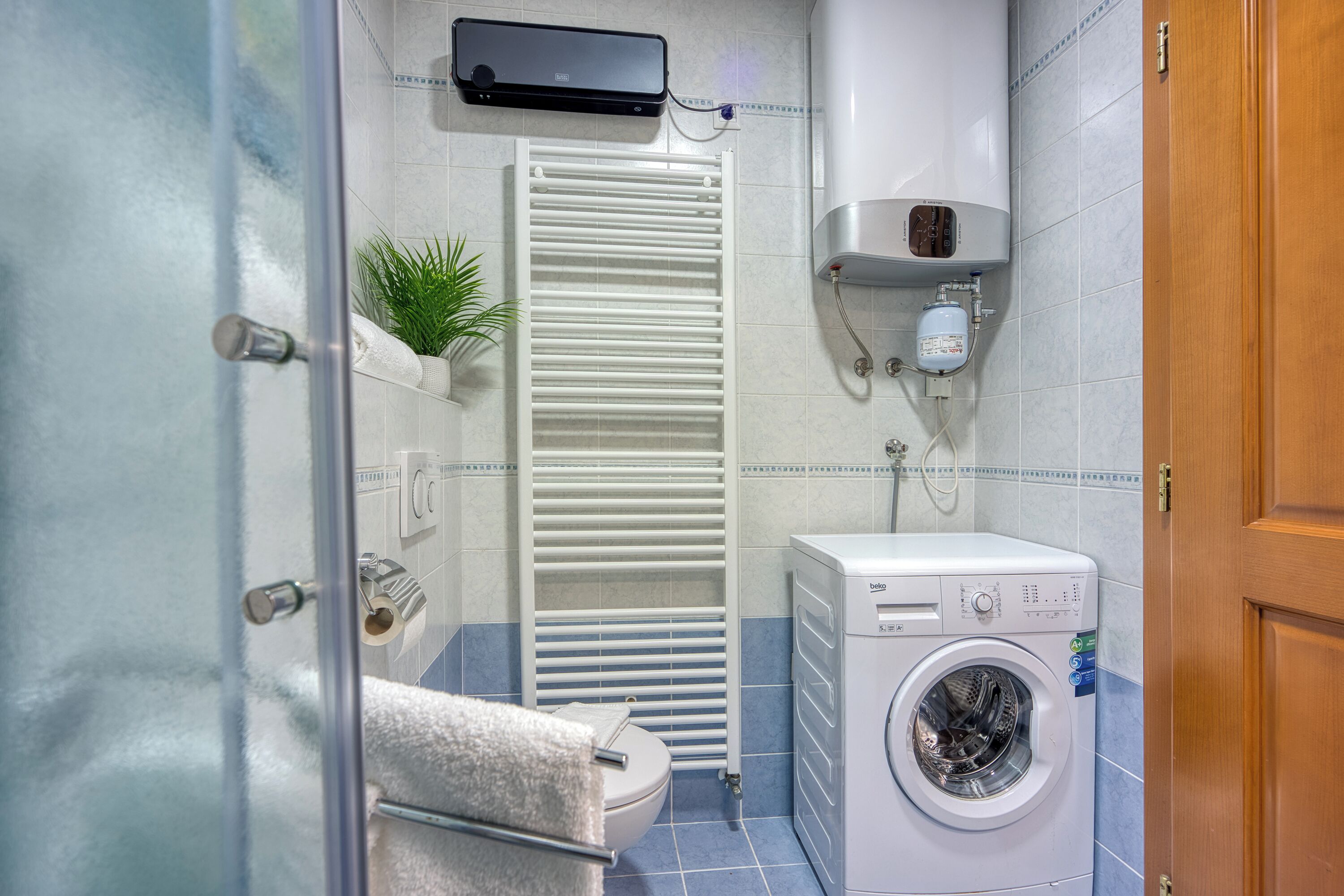 A compact bathroom with a toilet, a towel rack, a radiator, and a washing machine.