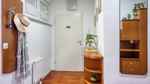 Un pasillo con una puerta de madera, un perchero con sombreros, un radiador y un espejo en la pared.