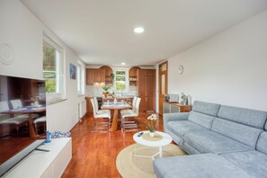 A modern kitchen with wooden cabinets, a dining area with a table and chairs, a grey sofa, and a small white table with a plant. - Sunset Gold Suite Portoroz Free Parking (Piran)