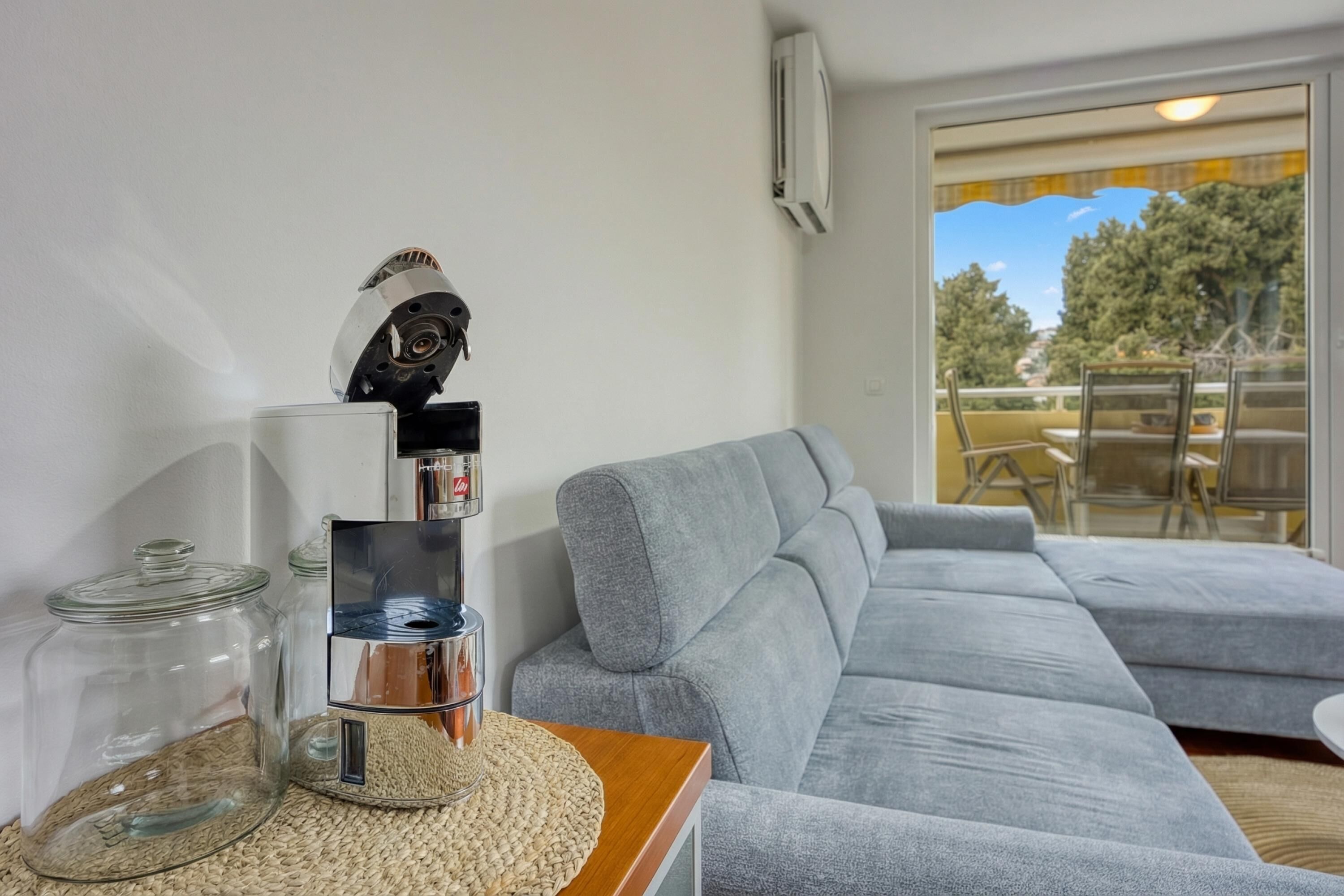 A modern living room with a grey sectional sofa, a coffee machine, and glass jars on a woven mat.