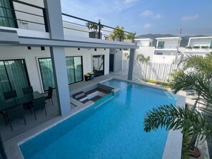 Une piscine extérieure moderne, dotée d’une balustrade en verre, d’un espace détente avec des chaises et offrant une vue sur les bâtiments voisins.