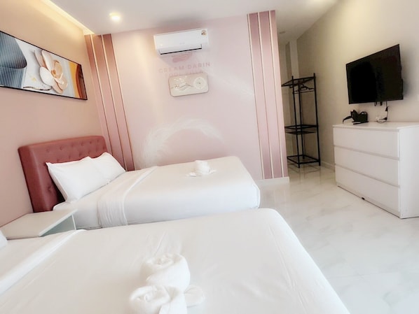 A hotel room with two beds, a white dresser, a TV, and an air conditioning unit.